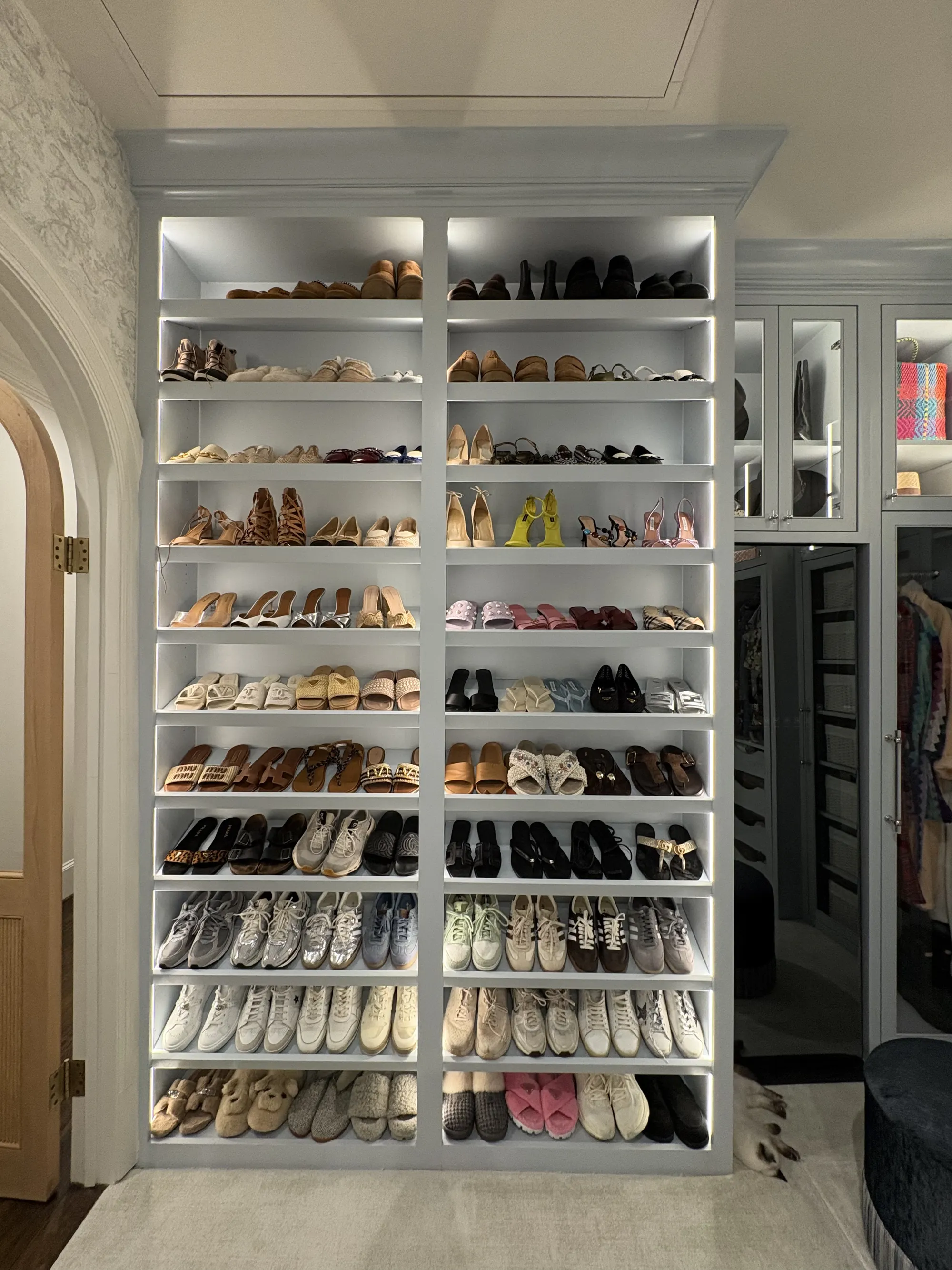 Lit built-in closet shelving lined with rows of shoes