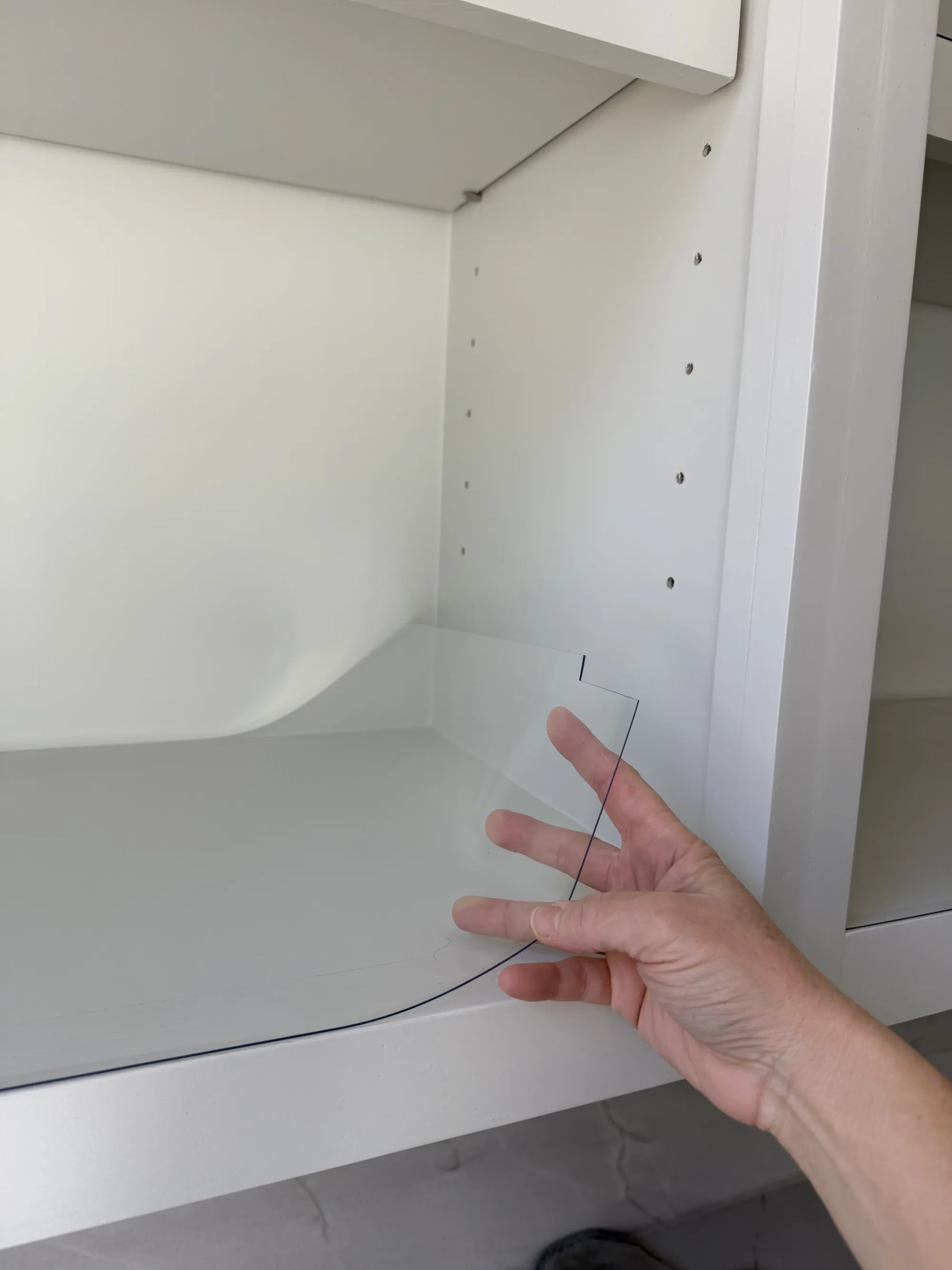 Hand fitting a clear liner onto a white cabinet shelf