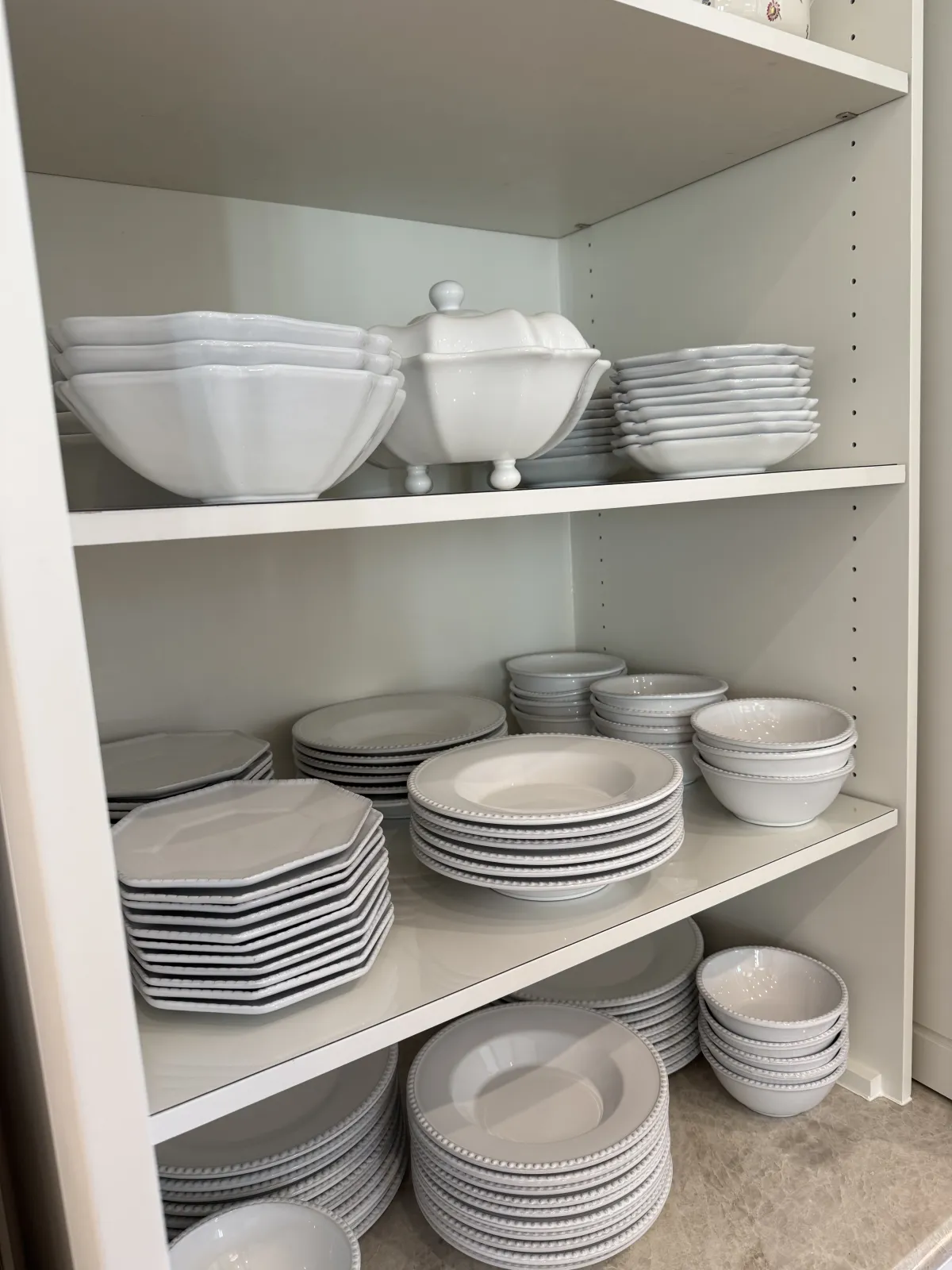 Stacks of white dinnerware on lined cabinet shelves