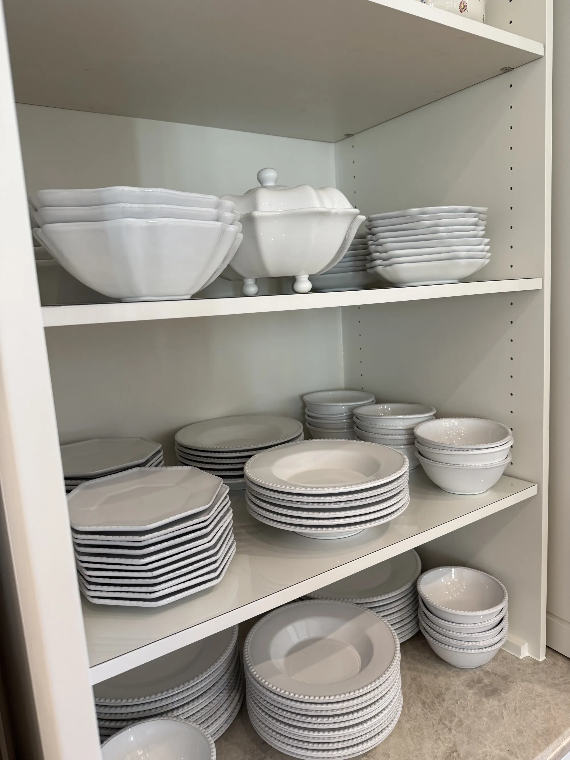 Stacks of white dinnerware on lined cabinet shelves